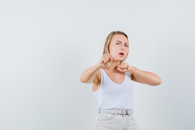 Blonde dame die zich in strijd bevindt stelt in hemd, broek en kijkt hatelijk, vooraanzicht.