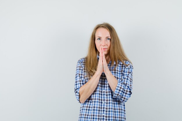 Blonde dame hand in hand in gebed gebaar in shirt en op zoek verstandig,