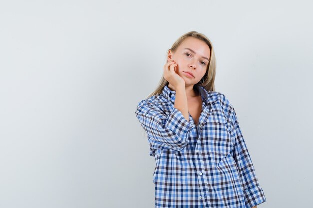 Blonde dame hand op de wang in casual shirt en op zoek verstandig