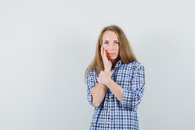 Blonde dame hand op de wang in shirt en op zoek rustig,