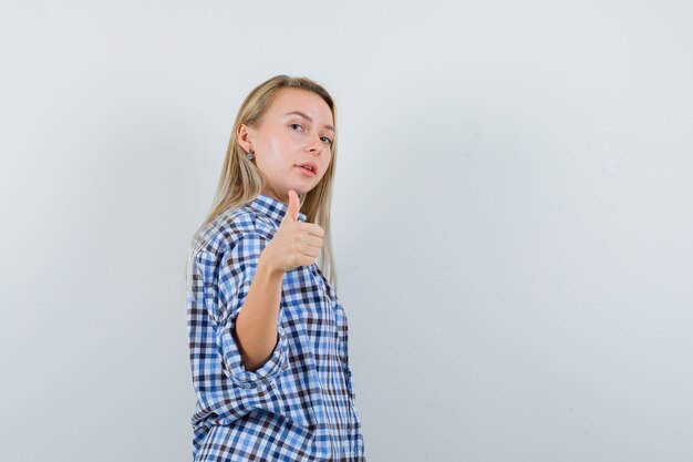 Blonde dame in casual overhemd duim opdagen en zelfverzekerd op zoek.