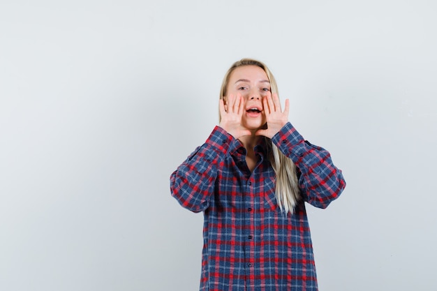 Blonde dame in casual overhemd schreeuwen of iets aankondigen en op zoek positief, vooraanzicht.