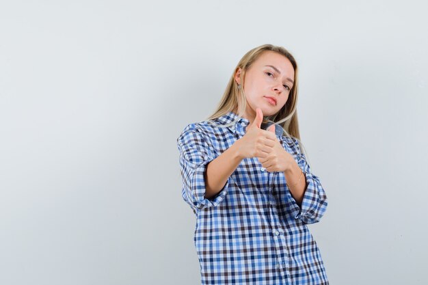 Blonde dame in casual shirt met dubbele duimen omhoog en op zoek naar zelfverzekerd