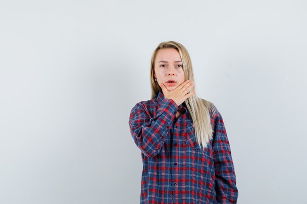 Blonde dame in casual shirt met hand op de kin en op zoek boos, vooraanzicht.