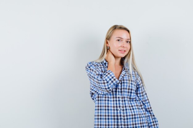 Blonde dame in geruit overhemd poseren met hand op nek en er mooi uitzien