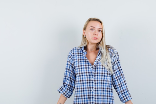 Blonde dame in geruit overhemd schouderophalend en kijkt verward