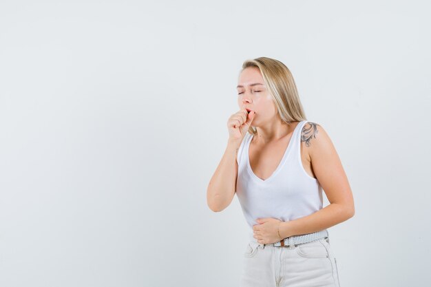 Blonde dame in hemd, broek die aan hoest lijdt en ziek kijkt, vooraanzicht.