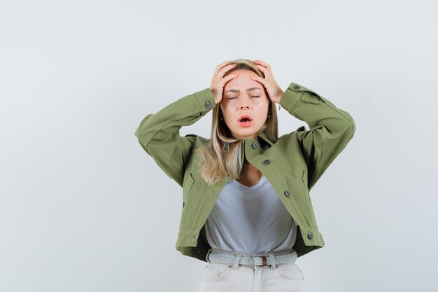 Blonde dame in jasje, broek hand in hand op het hoofd en treurig op zoek, vooraanzicht.