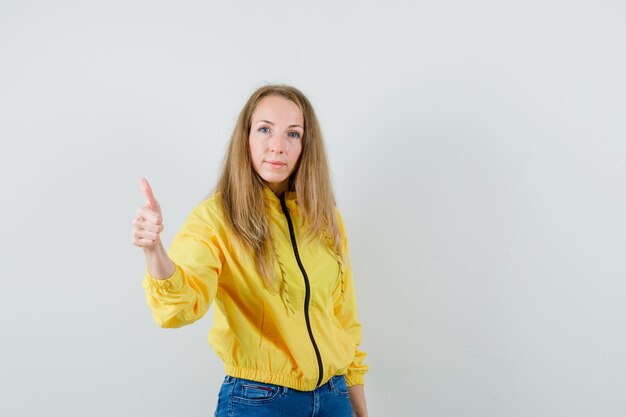 Blonde dame in jasje, spijkerbroek duim opdagen en er zelfverzekerd uitzien,