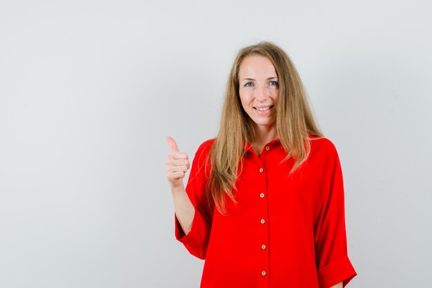 Blonde dame in rood shirt duim opdagen en joviaal kijken,