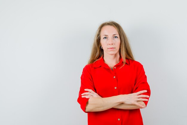 Blonde dame in rood shirt permanent met gekruiste armen en op zoek verstandig,