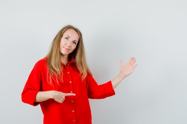 Blonde dame in rood shirt wijst naar de rechterkant en ziet er zelfverzekerd uit,