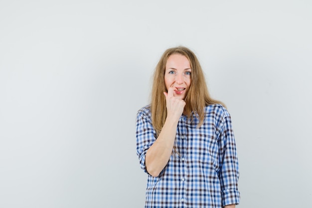 Blonde dame in shirt haar nagel bijten en beschaamd kijken,