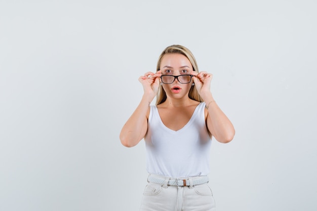 Blonde dame in singlet, broek die bril opstijgt en gefocust kijkt, vooraanzicht.