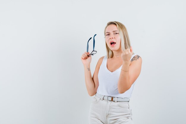 Blonde dame in singlet, broek met bril en op zoek naar geluk, vooraanzicht.