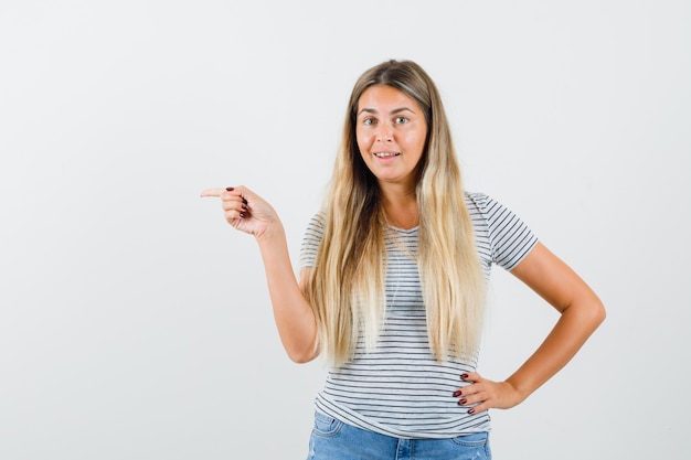 Blonde dame in t-shirt wijst opzij en kijkt gefocust, vooraanzicht.