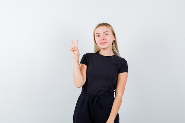 Blonde dame in zwarte jurk met V-teken en op zoek naar zelfverzekerd, vooraanzicht.