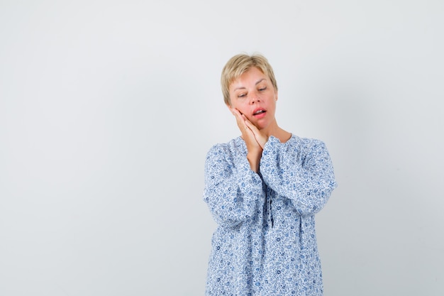 Blonde dame kussen gebaar maken in blouse met patroon en op zoek slaperig, vooraanzicht. ruimte voor tekst