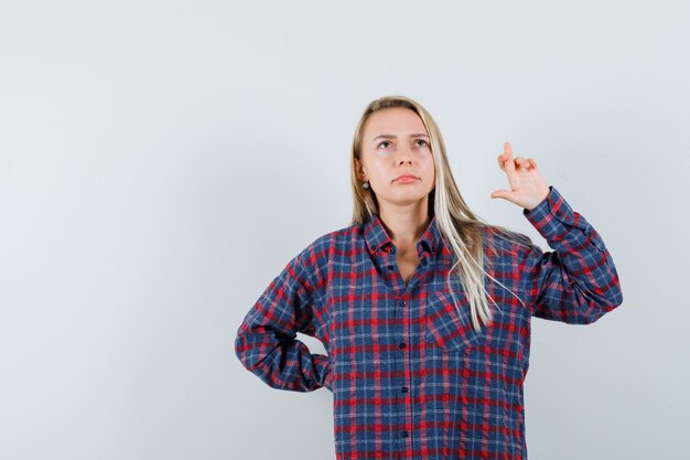 Blonde dame met vingers gekruist in casual shirt en aarzelend, vooraanzicht op zoek.