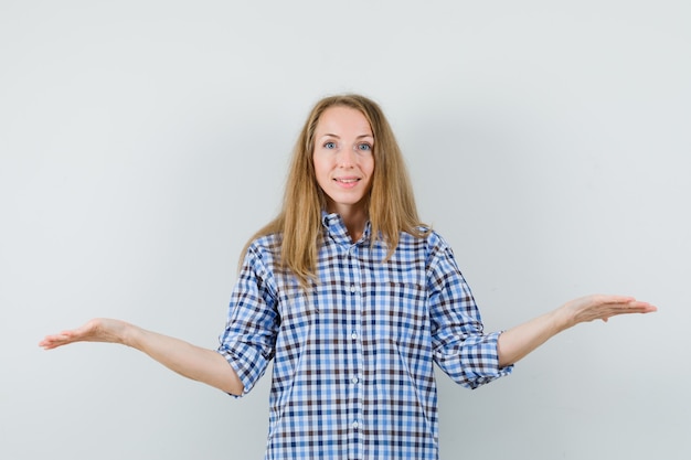 Blonde dame schalen gebaar maken in shirt en vrolijk kijken.