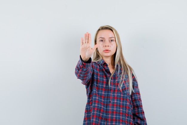 Blonde dame stop gebaar in casual shirt tonen en serieus kijken. vooraanzicht.