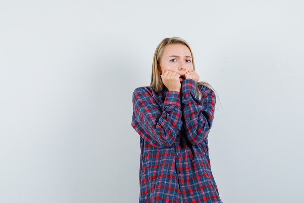 Blonde dame vuisten op wangen in casual shirt te drukken en bang op zoek. vooraanzicht.