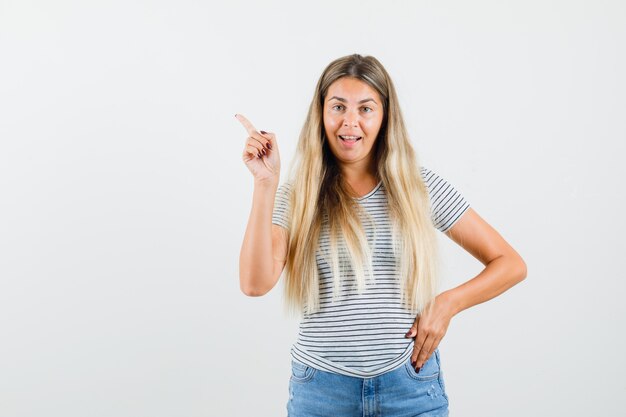 Blonde dame wijst terug terwijl ze in t-shirt praat en praatgraag. vooraanzicht.