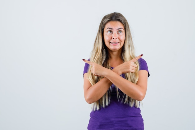 Blonde dame wijst weg in violet t-shirt en kijkt opgewonden, vooraanzicht.