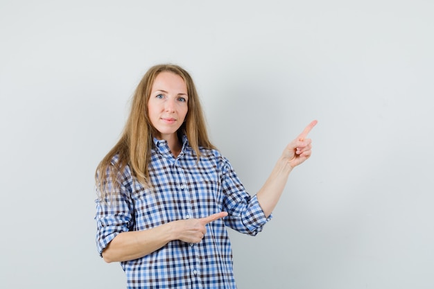 Blonde dame wijzend naar de rechterbovenhoek in shirt en kijkt zelfverzekerd,