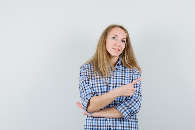 Blonde dame wijzend naar de rechterbovenhoek in shirt en kijkt zelfverzekerd,