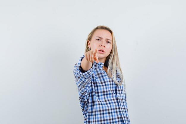 Blonde dame wijzend op camera in casual shirt en op zoek zelfverzekerd