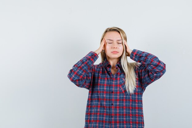 Blonde dame wrijft over haar slapen in een casual shirt en kijkt uitgeput, vooraanzicht.