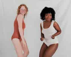 Gratis foto blonde en afrikaanse jonge vrouwen die samen tegen grijze achtergrond dansen