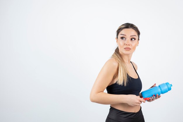 Blonde fitte vrouw in zwarte top die een fles water met expander vasthoudt.