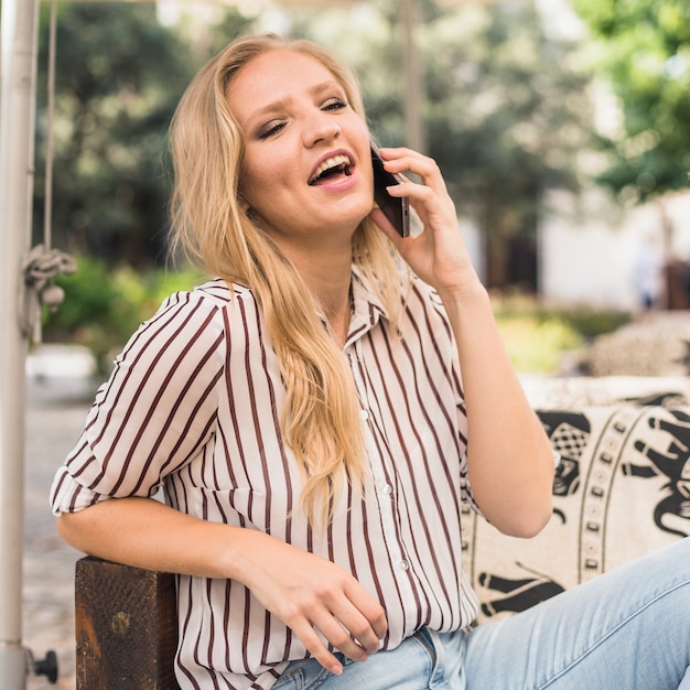 Blonde jonge vrouw die lacht tijdens het praten op mobiele telefoon