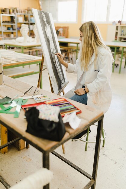 Blonde jonge vrouw die op canvas in workshop schetsen