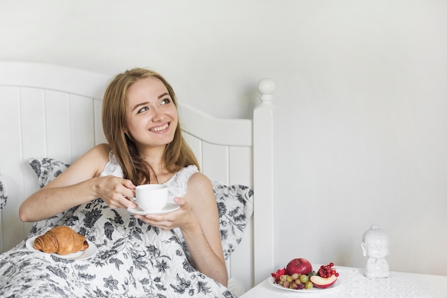 Blonde jonge vrouw die van het ochtendontbijt op bed geniet