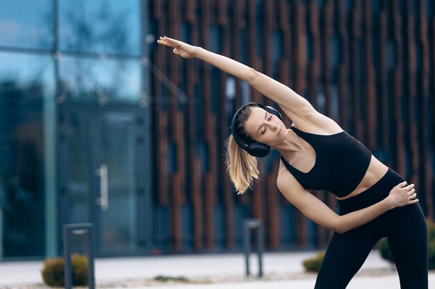 Blonde jonge vrouw die zich uitstrekt met opgeheven hand in park