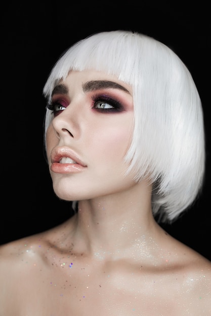 Blonde jonge vrouw met modieuze make-up die op zwarte achtergrond wordt geïsoleerd