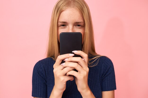 Blonde jonge vrouw met vernauwende ogen, met een verdachte blik met mobiel