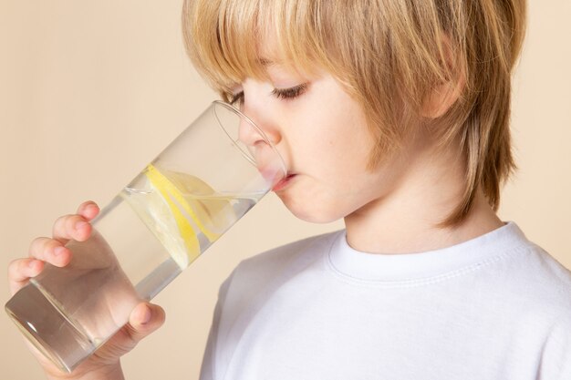 Gratis foto blonde jongen klein schattig drinken citroensap op roze muur