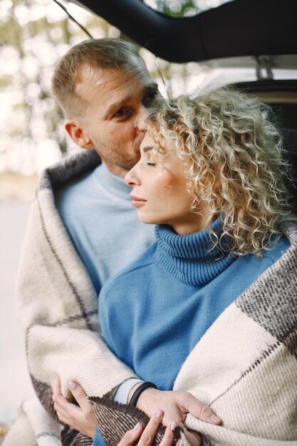 Blonde krullende vrouw en man zitten in een kofferbak in de auto in het herfstbos