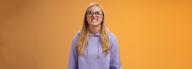 Gratis foto blonde meisje toont tanden waarschuwt kan zichzelf staan bijten dwaas rond grimacing grappig dragen van paarse hoodie