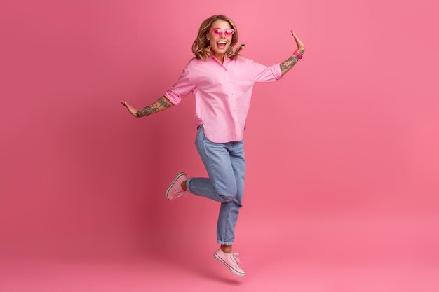 Blonde mooie vrouw in roze shirt en spijkerbroek glimlachend springen