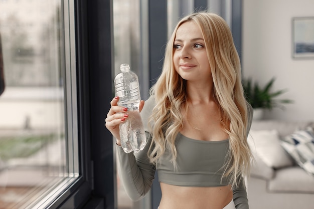 Blonde poseren. Dame in een sportpak. Vrouw thuis bij het raam.