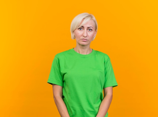 Blonde Slavische vrouw die op middelbare leeftijd voorzijde bekijkt die op gele muur met exemplaarruimte wordt geïsoleerd