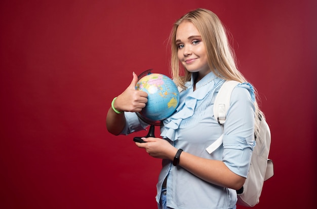 Blonde studentenvrouw houdt een wereldbol vast en ziet er positief uit.