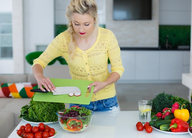 Gratis foto blonde vrouw bereidt salade voor in de keuken