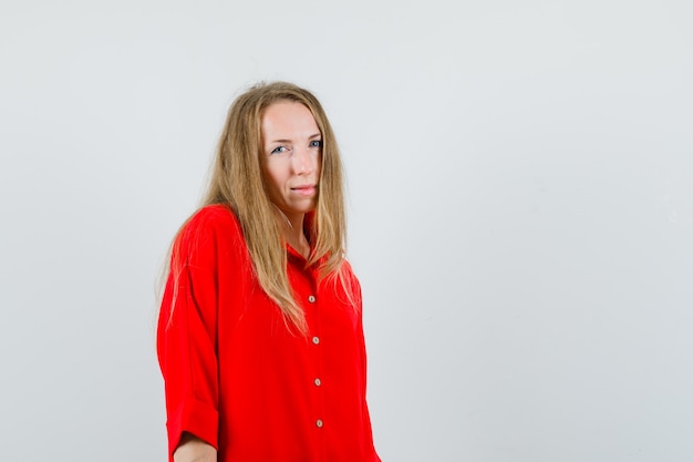 Blonde vrouw camera in rood shirt kijken en op zoek twijfelachtig,