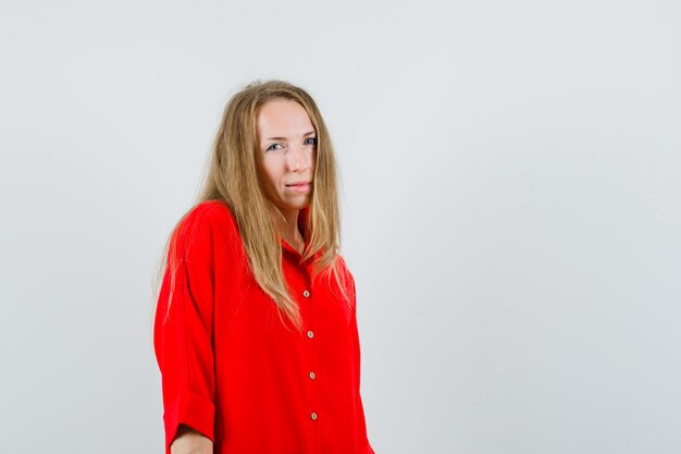 Blonde vrouw camera in rood shirt kijken en op zoek twijfelachtig,